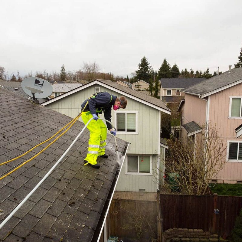 gutter cleaning professional spraying inside gutter in yellow trousers