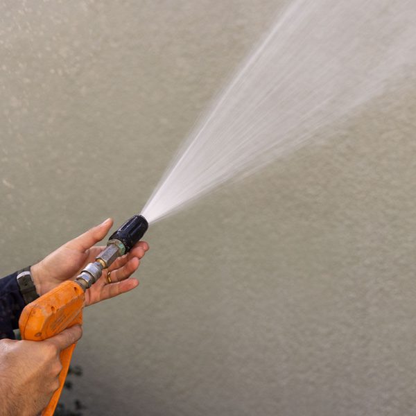 pressure washing professional spraying house siding with orange sprayer