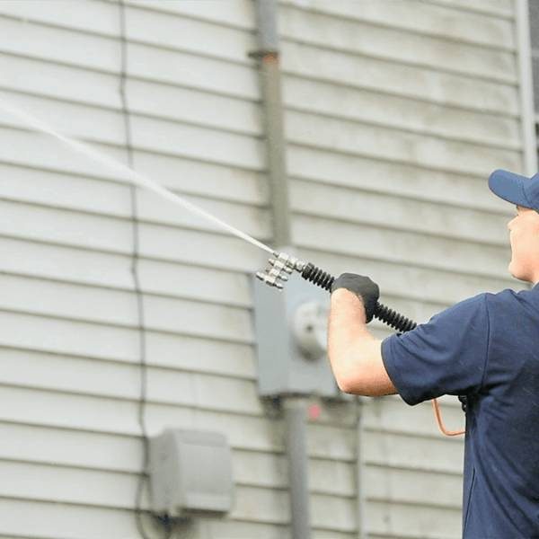 pressure washing professional cleaning side of home in blue shirt and hat