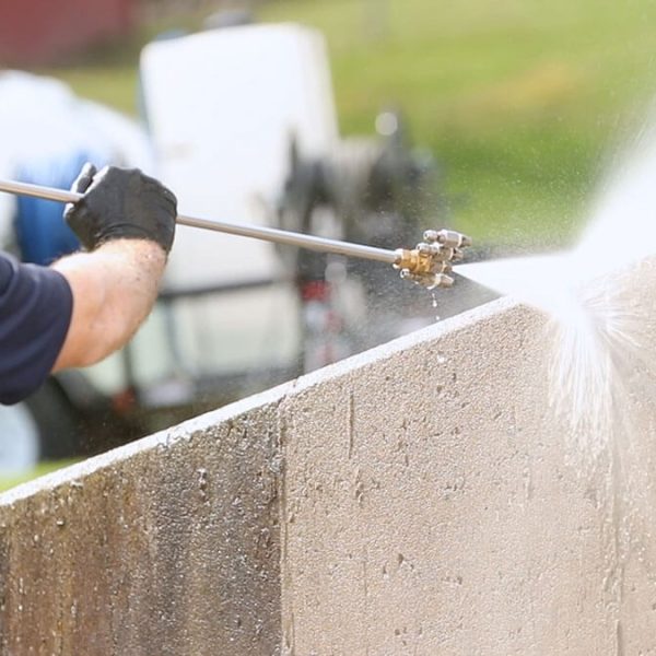 pressure washing professional washing concrete wall in blue shirt