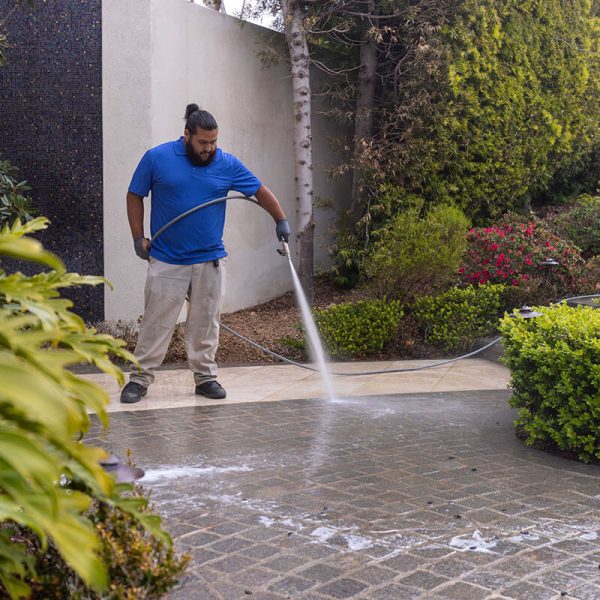 pressure washing professional washing pavers in blue shirt