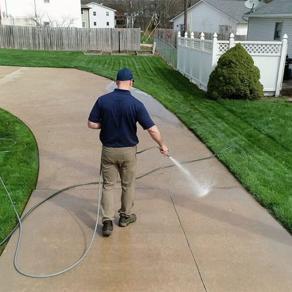 pressure washing professional washing concrete in front of white home