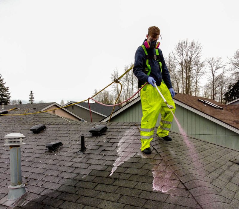 pressure washing professional washing roof of home in yellow work trousers